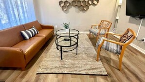 Un salon avec un canapé en cuir marron, deux fauteuils en bois, une table basse ronde et une étagère hexagonale fixée au mur.