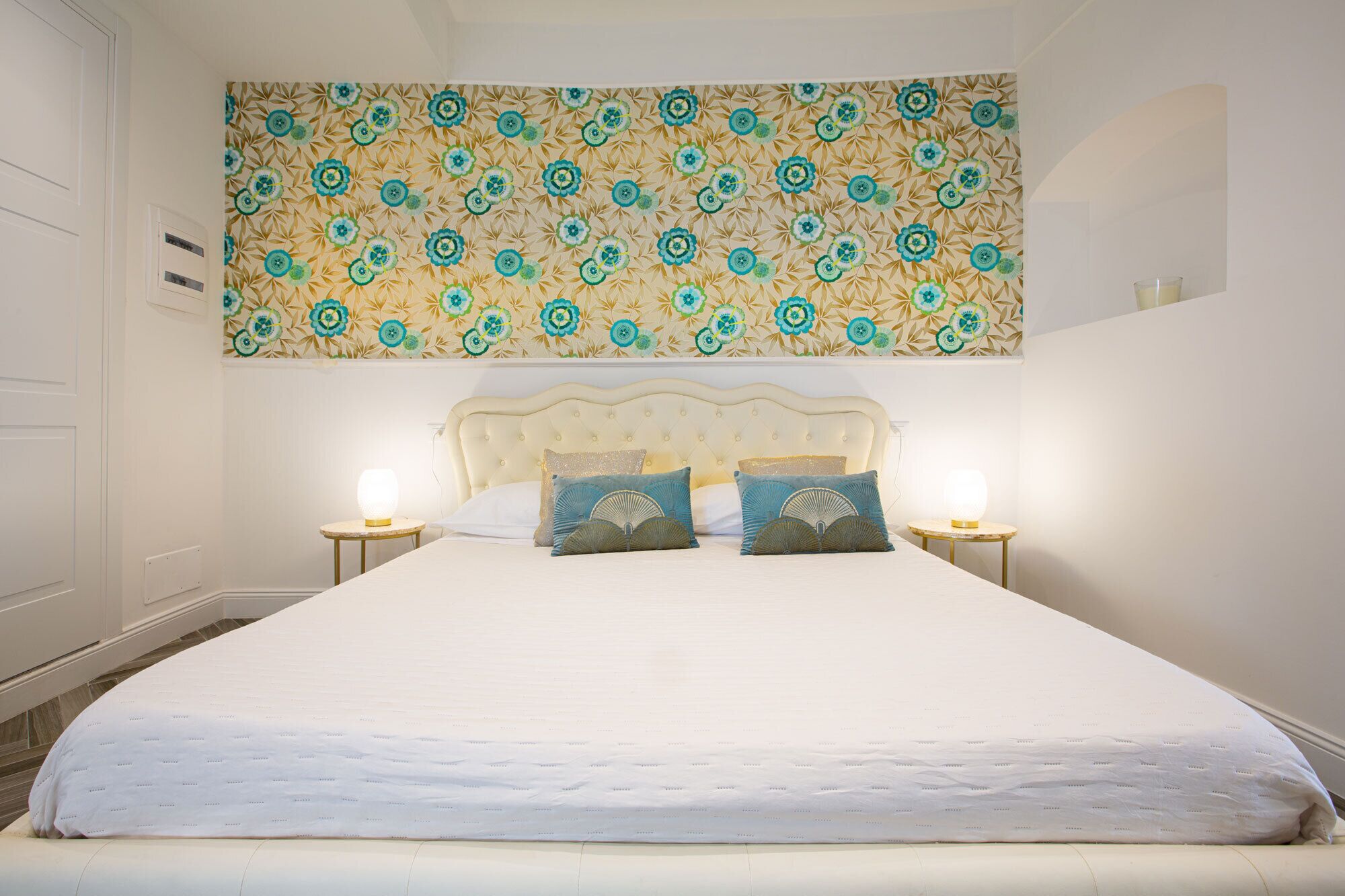 A neatly made bed with a white duvet, two decorative pillows, and two bedside lamps.