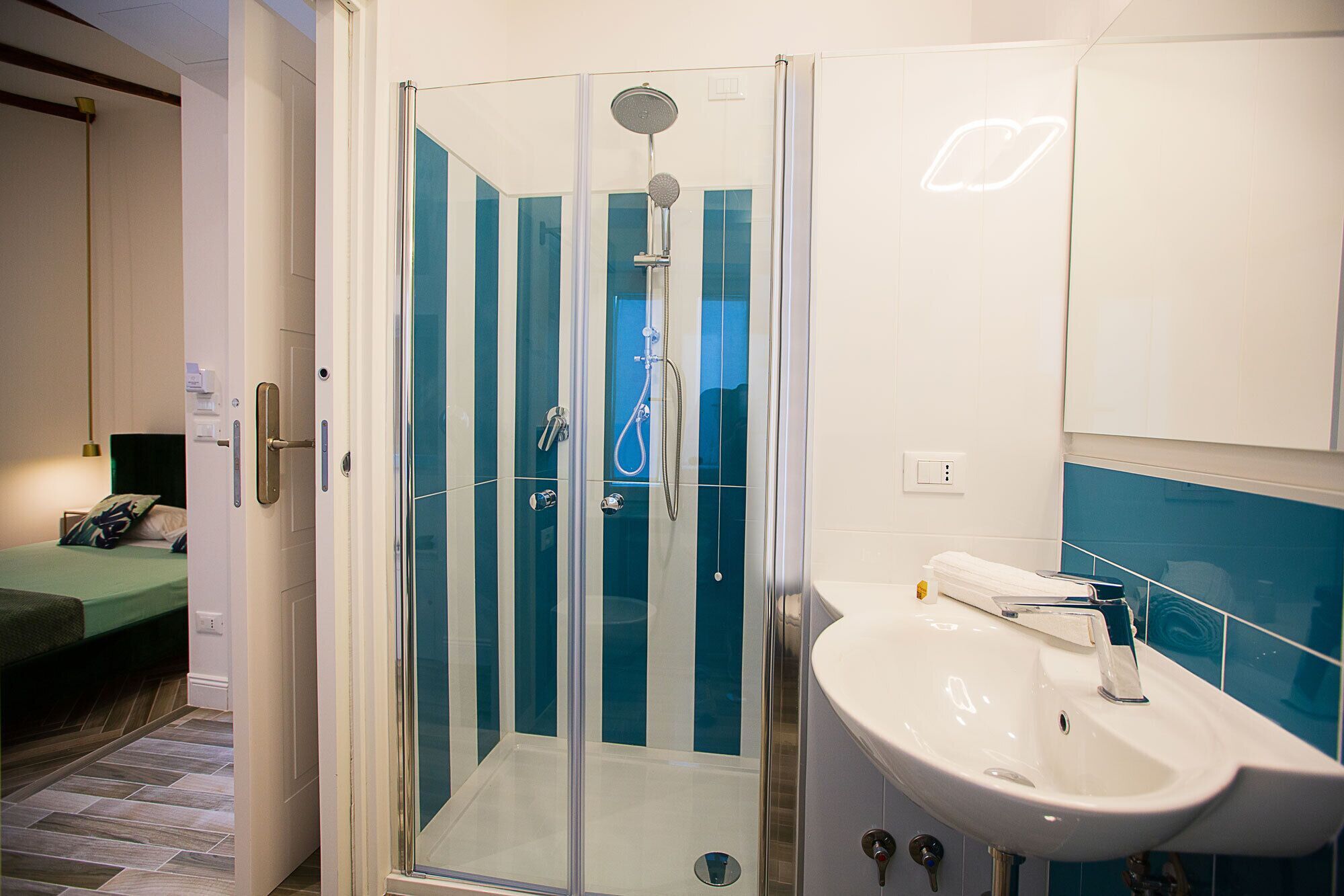Un bagno moderno con doccia vetrata, un lavandino bianco e un letto nella stanza adiacente.