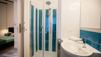 Un bagno moderno con doccia vetrata, un lavandino bianco e un letto nella stanza adiacente.