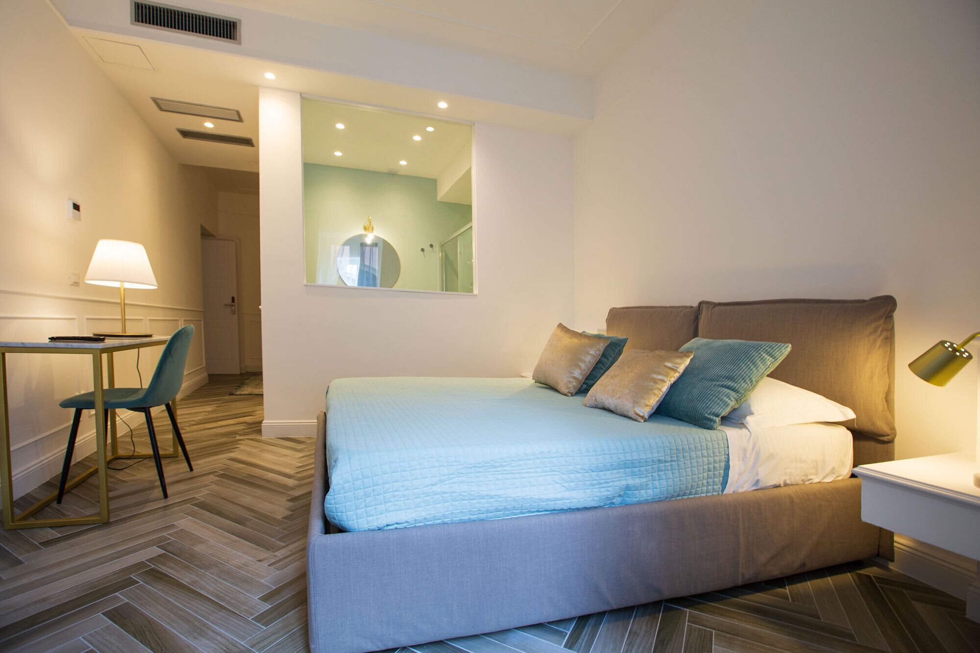 A hotel room with a bed, a desk, a chair, and a mirror.