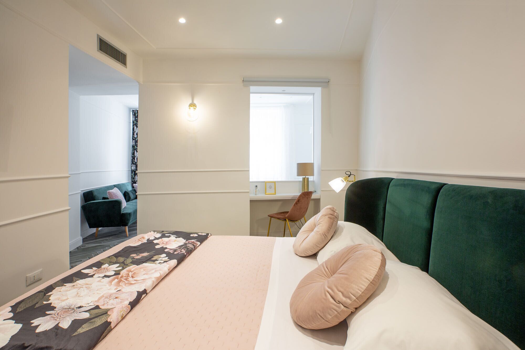 Une chambre d’hôtel avec un lit, une tête de lit recouverte d’un tissu vert, une fenêtre donnant sur un paysage agréable et un bureau avec une lampe.