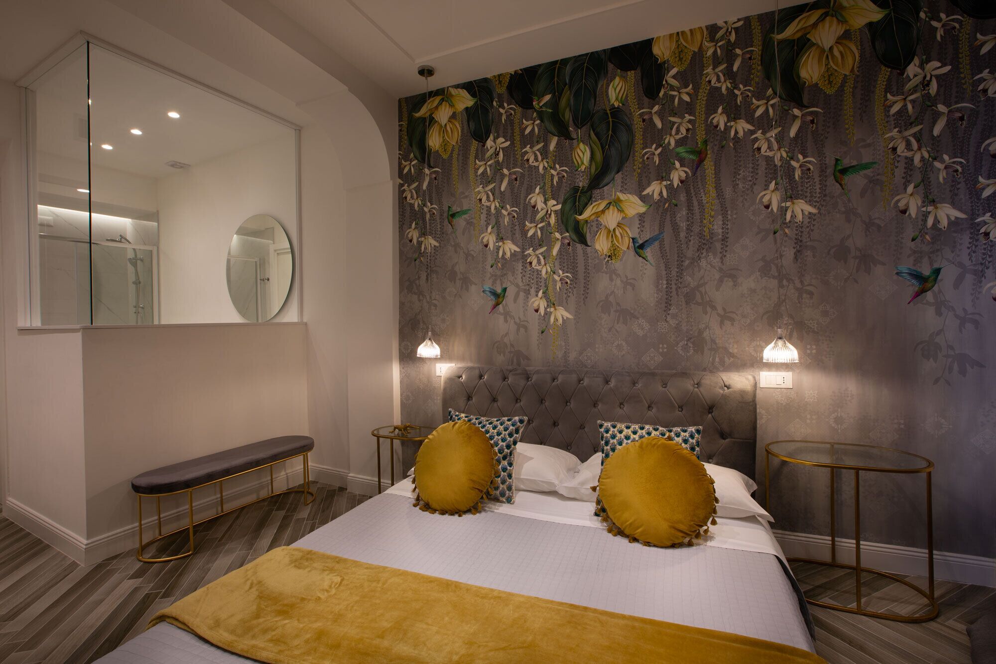 A bedroom with a tufted headboard, a large mirror, a bench, and a bed with patterned pillows and a yellow throw.