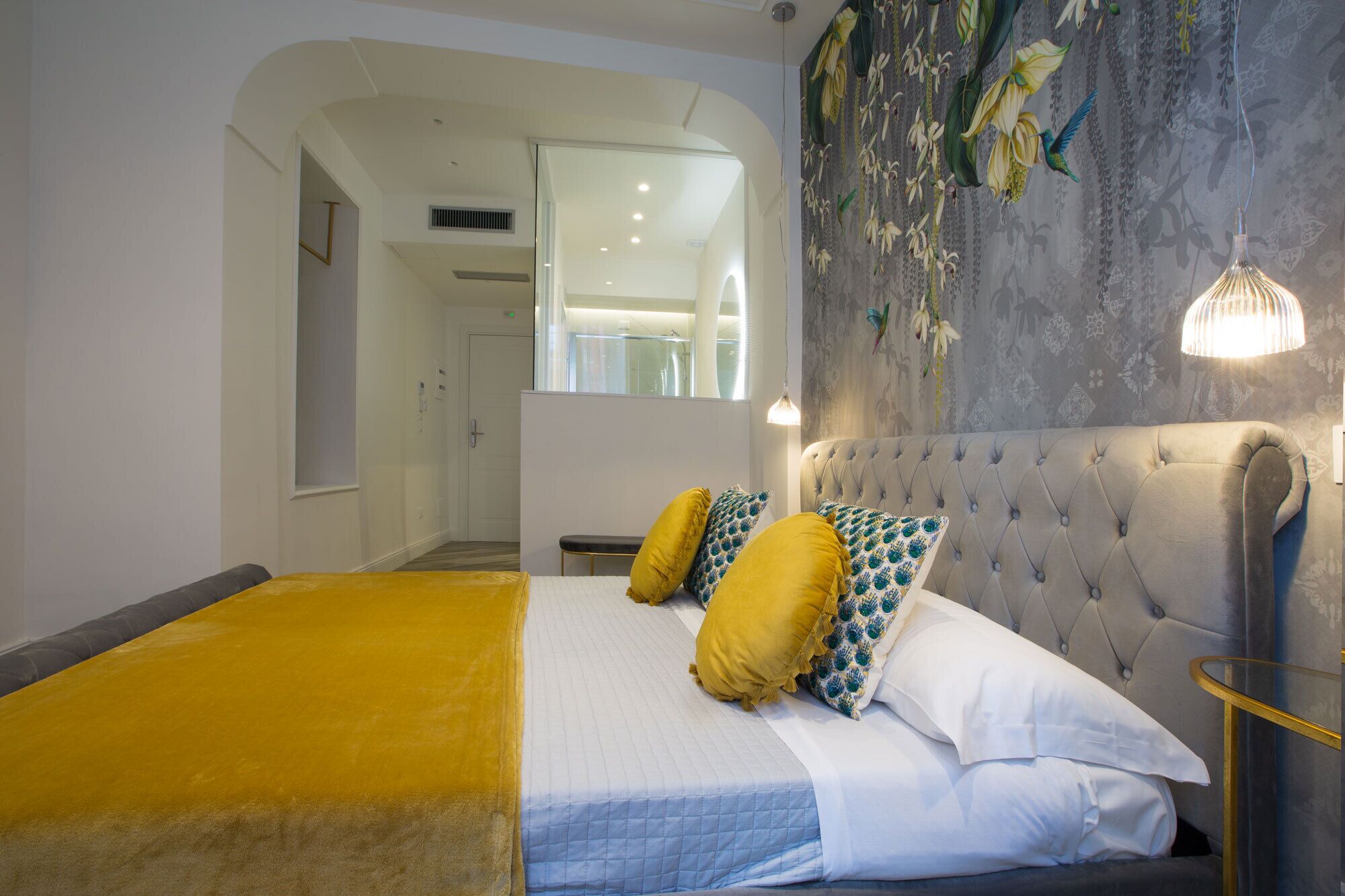 Ein Schlafzimmer mit einem Bett, einer gesteppten Kopfteil und einer Wand mit floralem Muster.