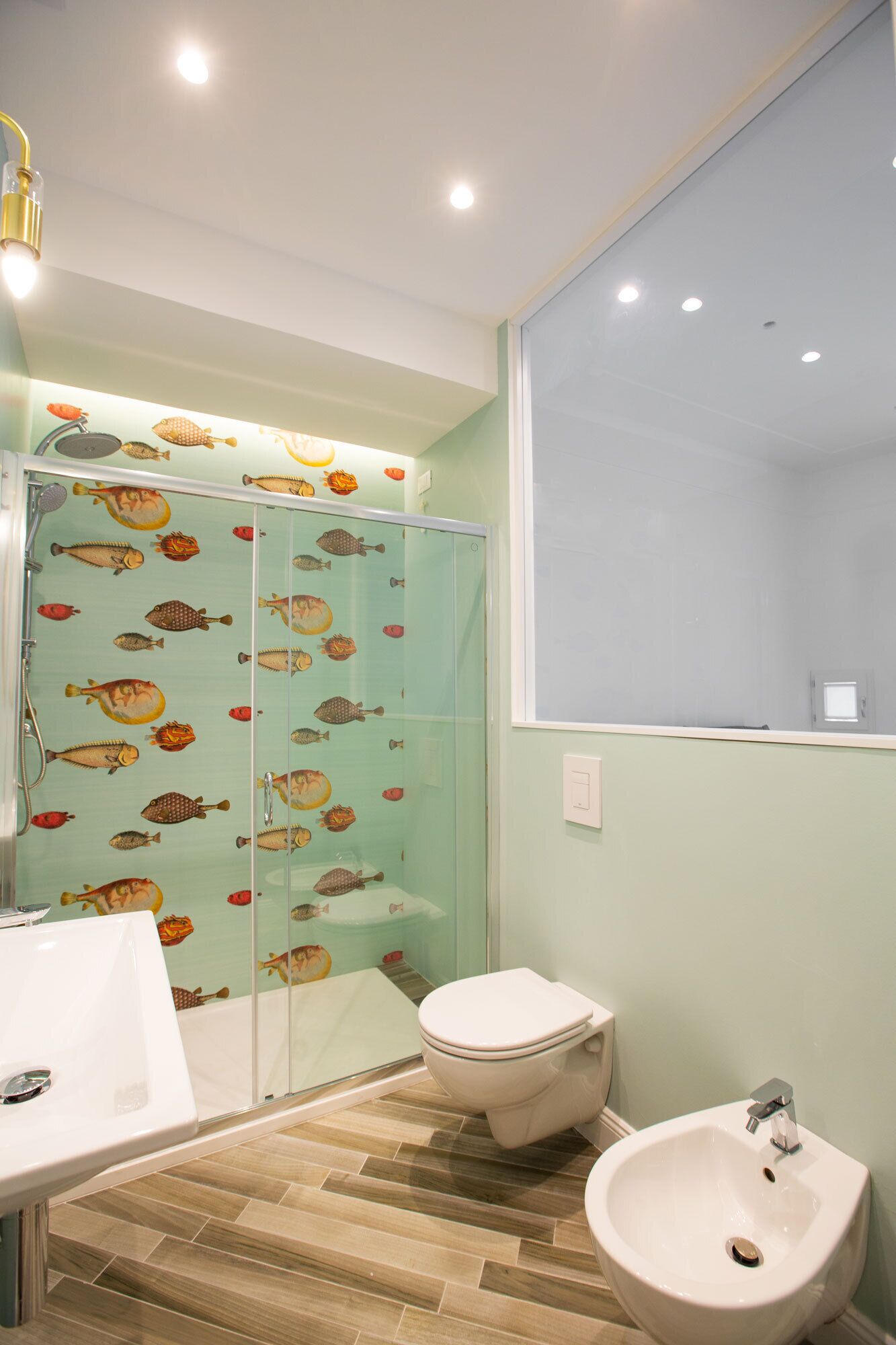 A bathroom with a glass shower enclosure, a toilet, a sink, and a bidet.