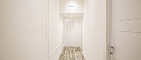 A narrow hallway with a wooden floor and white walls.
