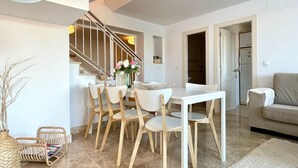 Una sala moderna con comedor, una escalera y una cocina visible a través de un vano abierto.