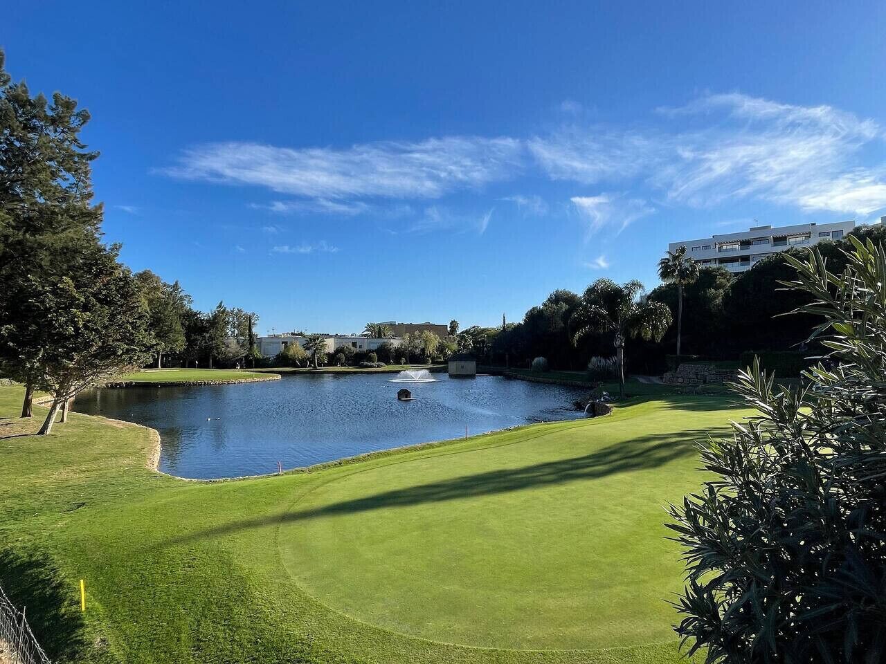 En golfbane med en sø, træer og en bygning i baggrunden.