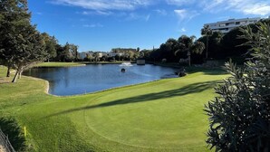 Un campo de golf con un estanque, árboles y un edificio al fondo.