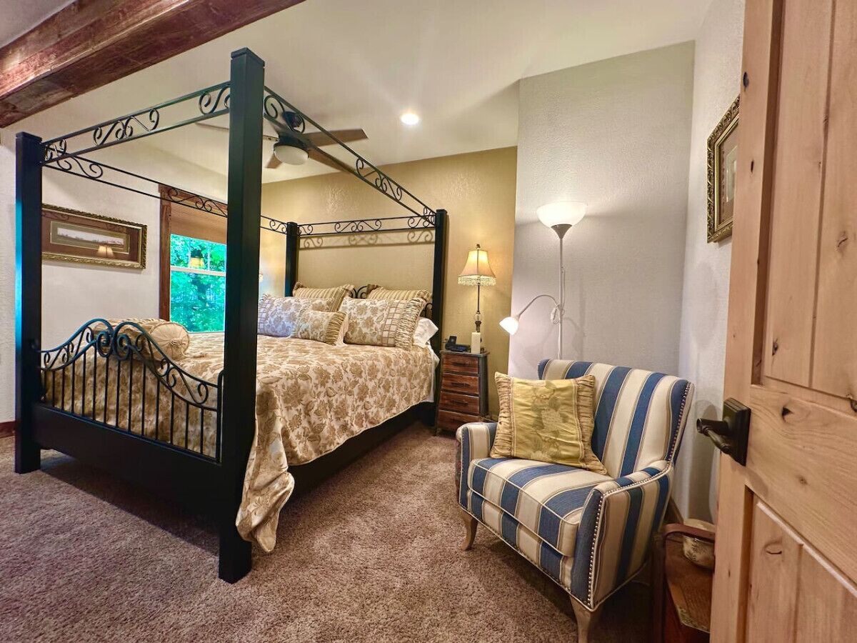A bedroom with a four-poster bed, a striped armchair, a nightstand, and a wooden wardrobe.