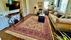 Un salon avec un grand tapis, un canapé, un téléviseur et une petite table sur laquelle se trouve une lampe.