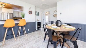 A dining area with a wooden table set for four, surrounded by black chairs. There is a kitchen with white cabinets and a stainless steel refrigerator in the background. - Island Cottage w/ Pool Table & Walking distance to Cranberry!  (Huntsville)