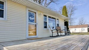 A single-story house with a wooden deck, a sliding glass door, and a porch with two rocking chairs. - Island Cottage w/ Pool Table & Walking distance to Cranberry!  (Huntsville)