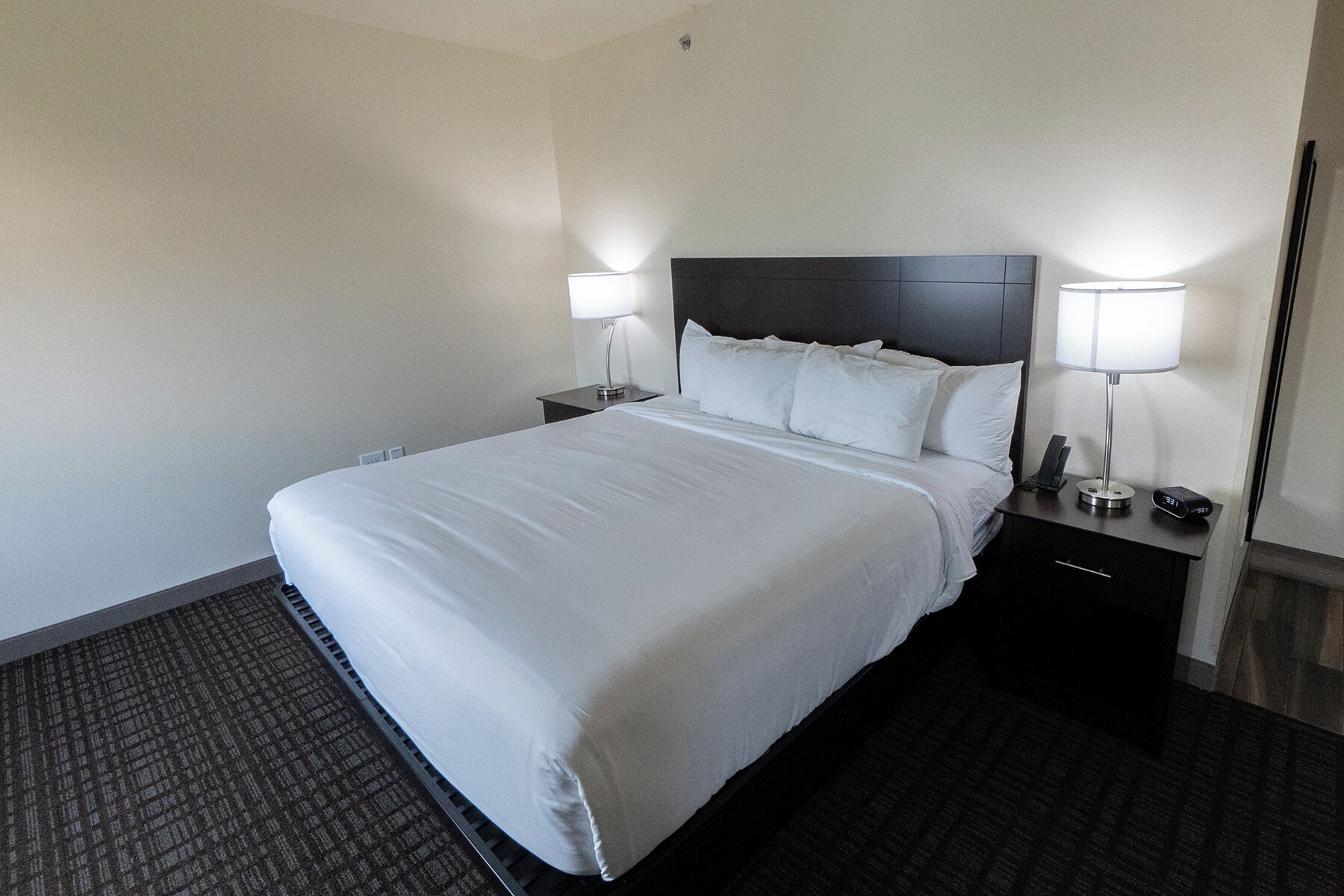 A hotel room with a large bed, two bedside tables with lamps, and a dark headboard.