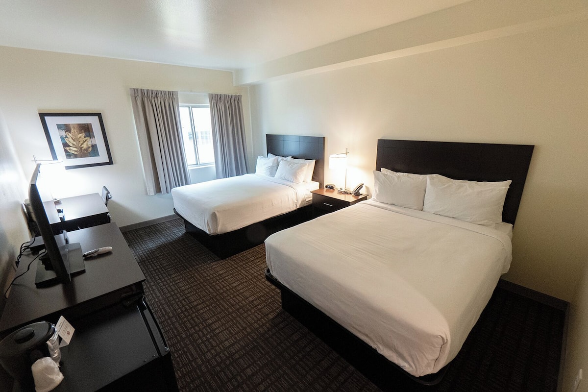 A hotel room with two beds, a desk with a computer, a lamp, and a framed picture on the wall.