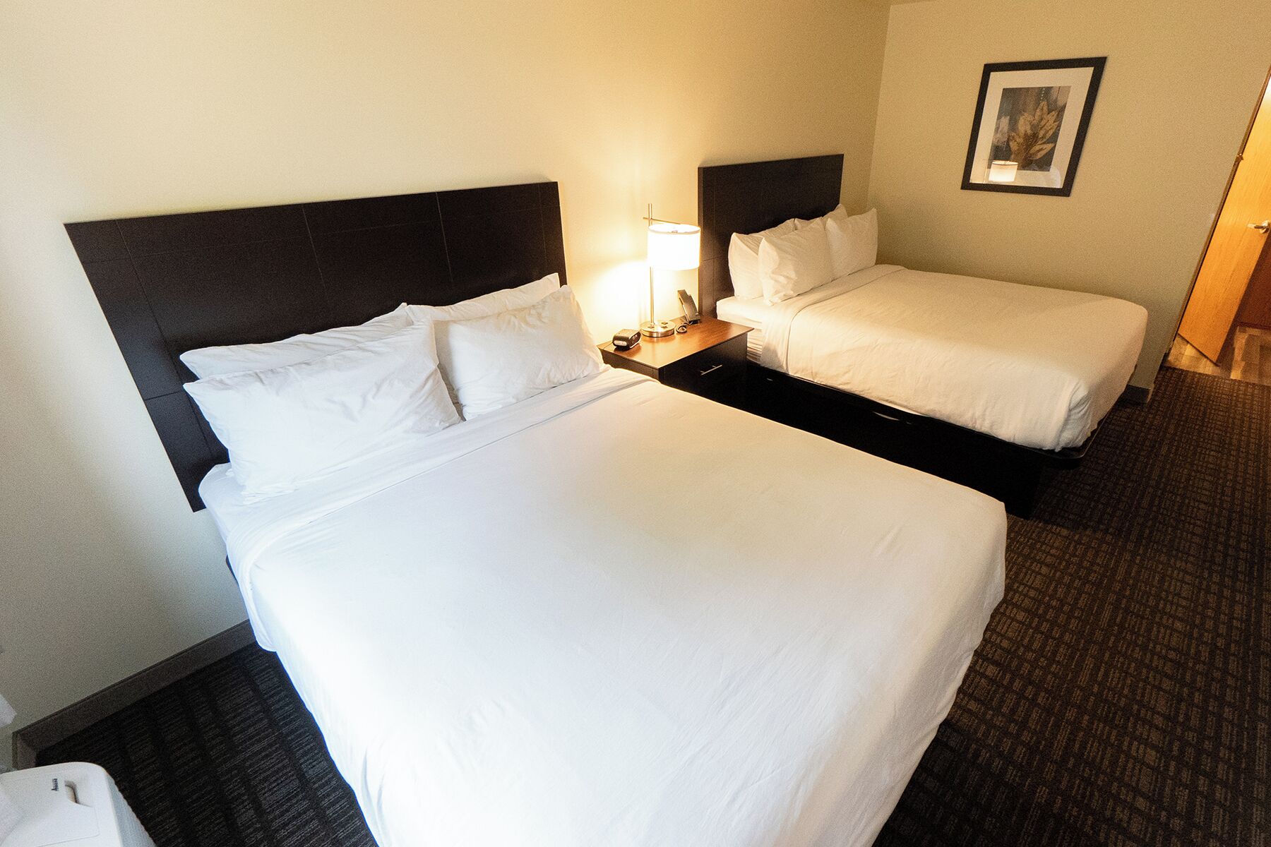 A hotel room with two beds, a nightstand with a lamp, and a framed picture on the wall.