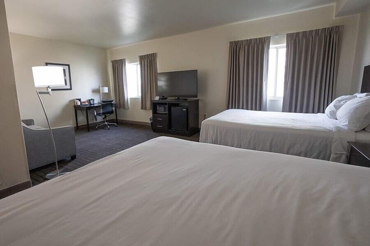 A hotel room with two beds, a desk with a chair, a television, and a desk lamp.