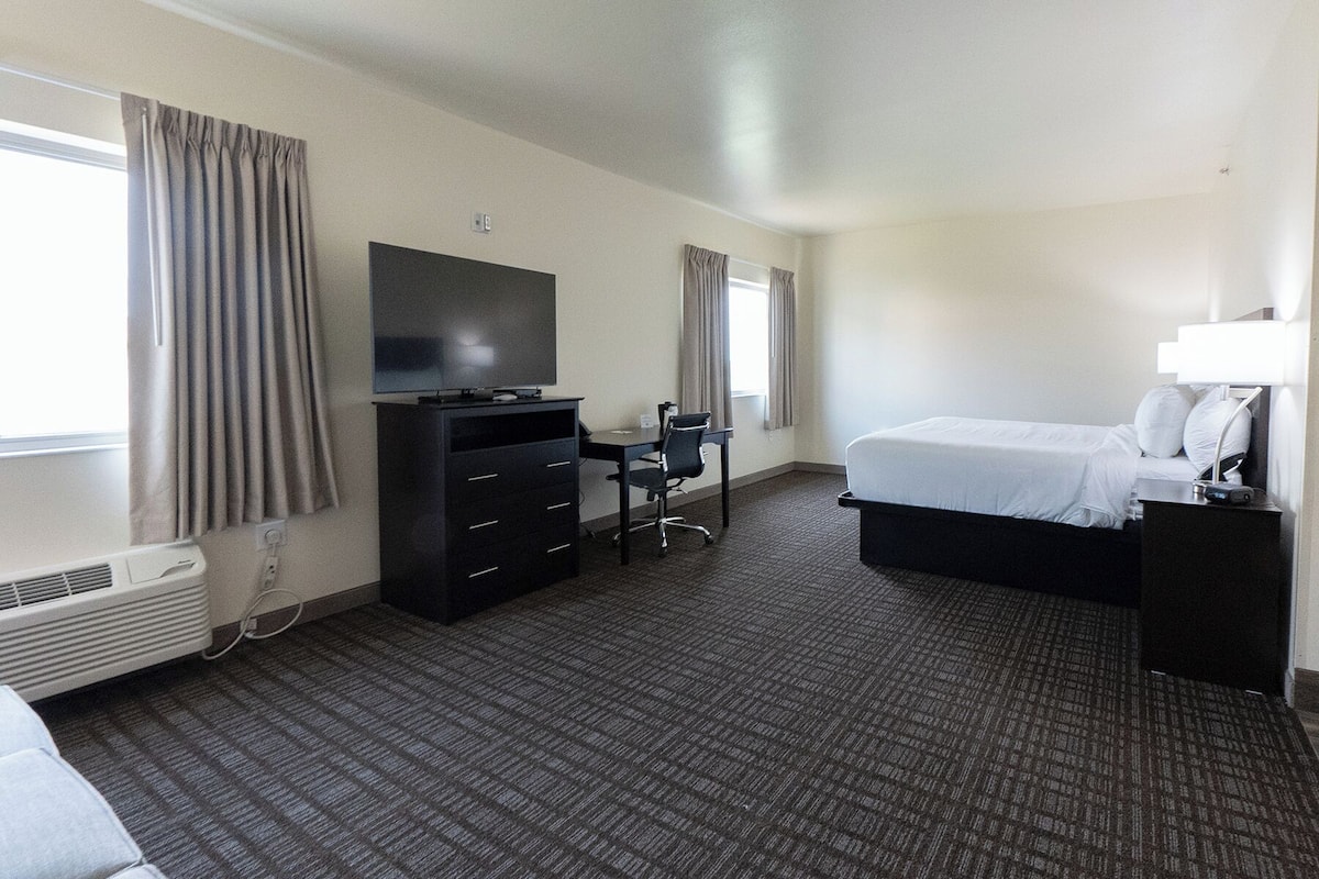A hotel room with a bed, a desk with a chair, a television, and a wardrobe.