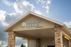 Exterior del Cobblestone Inn & Suites, con fachada de piedra y cielo despejado.