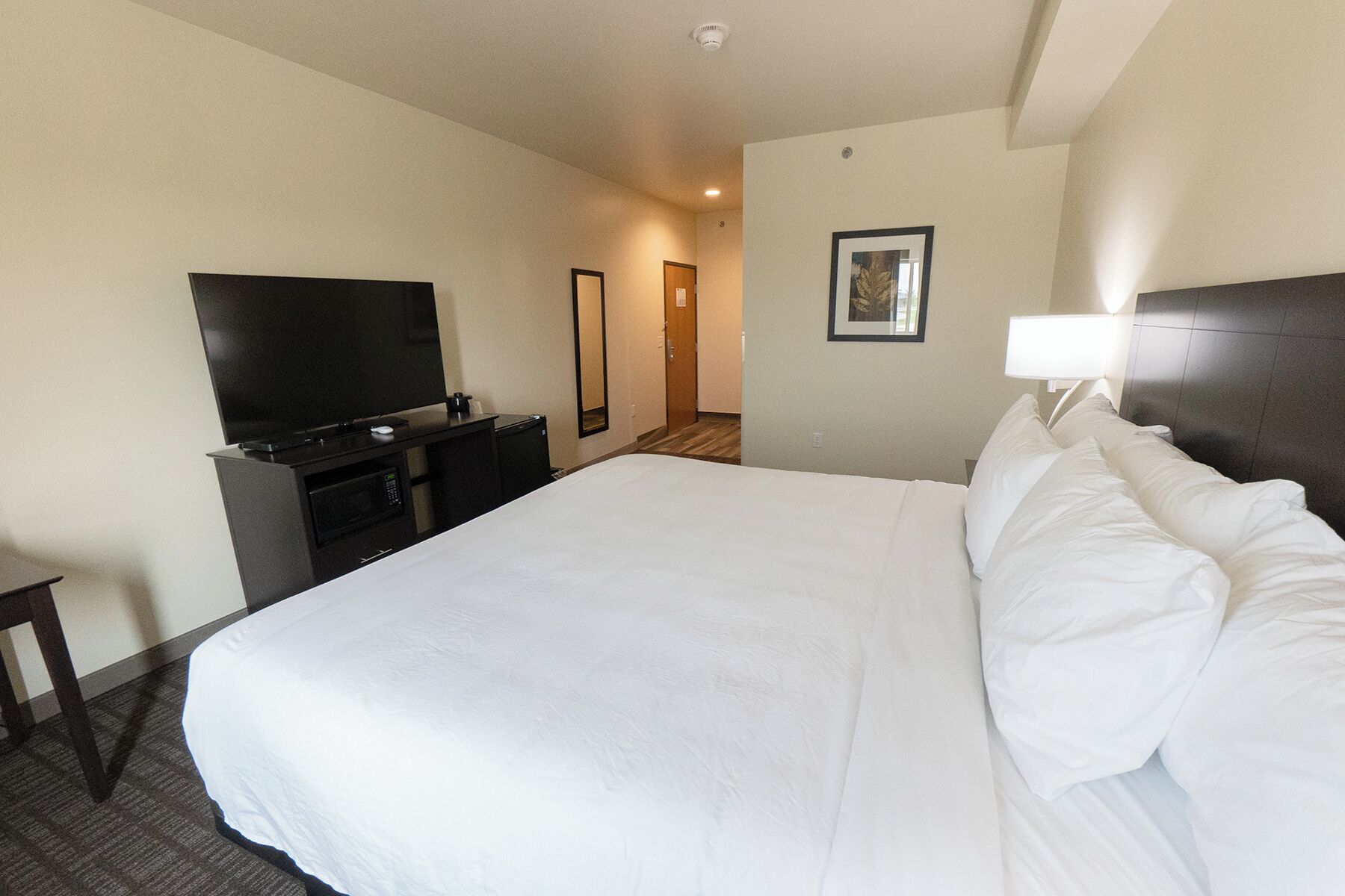 Quarto de hotel com uma cama grande, televisão de tela plana, escrivaninha com micro-ondas e porta que dá para outro quarto.