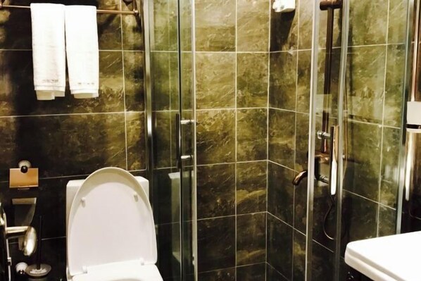A bathroom with a toilet, a shower area with glass doors, and a sink. - Nanyi Hotel (Chishui)