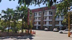 A multi-story building with a red sign, parked cars, and palm trees. - Nanyi Hotel (Chishui)