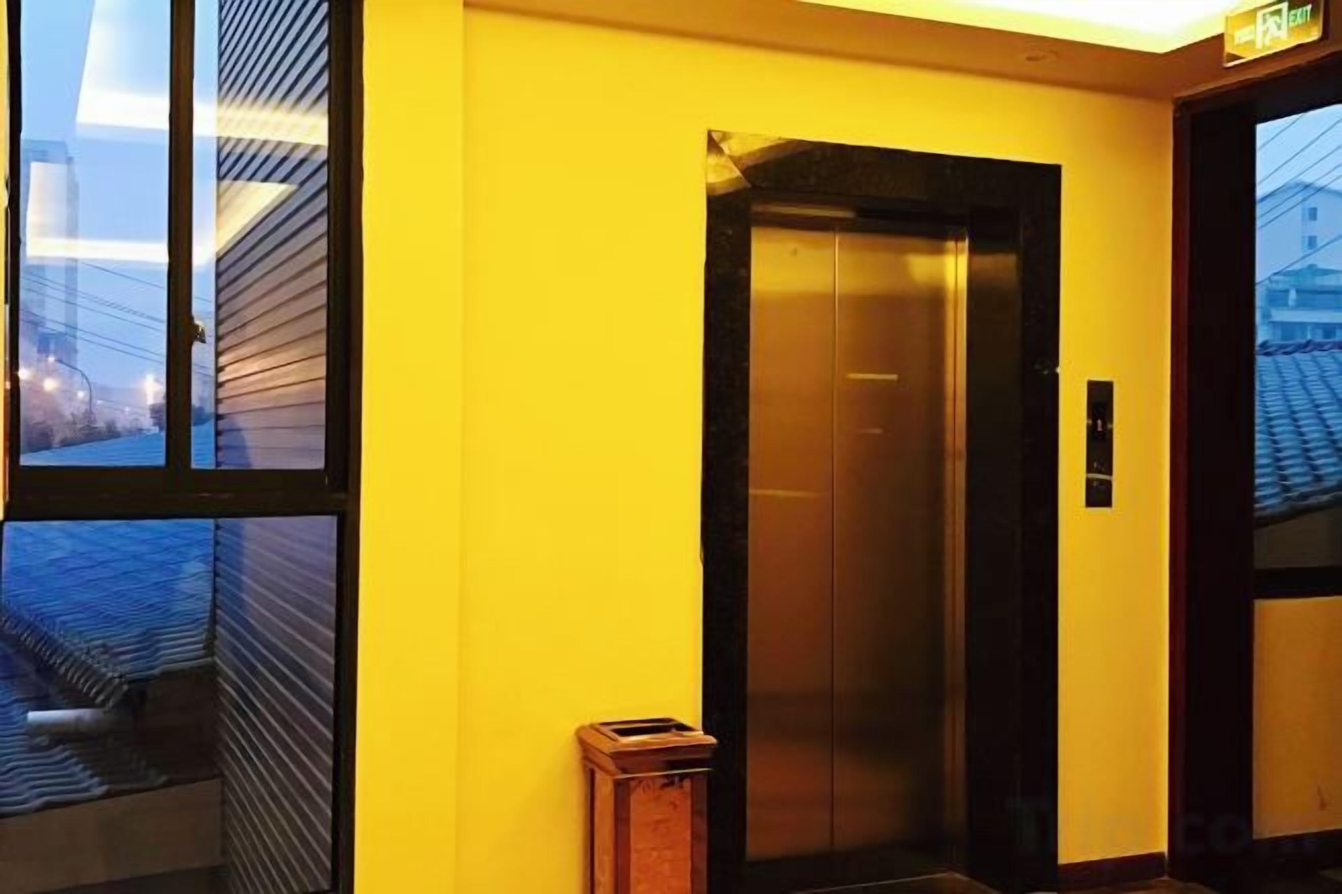 An elevator in a building with a yellow wall and a window showing a cityscape.