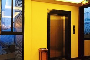 Um elevador em um prédio com parede amarela e janela com vista para a paisagem urbana.