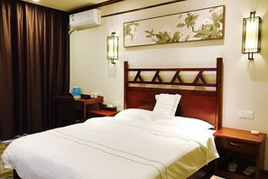 A hotel room with a large bed, a wooden headboard, two bedside tables, a desk with a lamp, and a wall-mounted air conditioner. - Nanyi Hotel (Chishui)