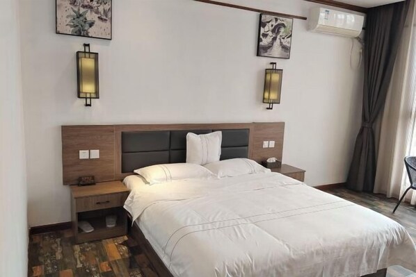 A hotel room with a bed, bedside tables, wall-mounted lights, artwork, and an air conditioning unit. - Nanyi Hotel (Chishui)