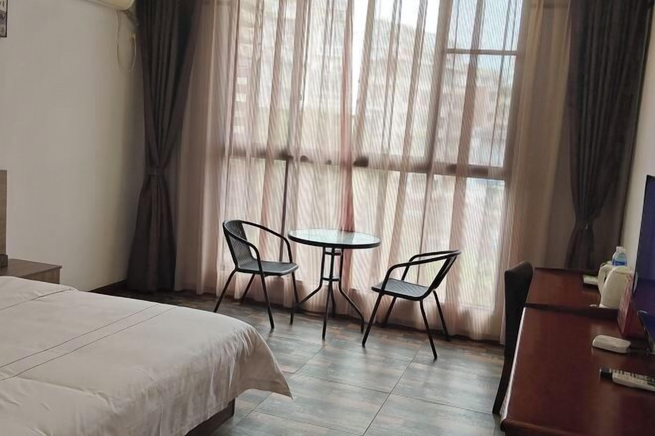 A hotel room with a bed, a small round table with two chairs, a desk with a chair, and a window with curtains.