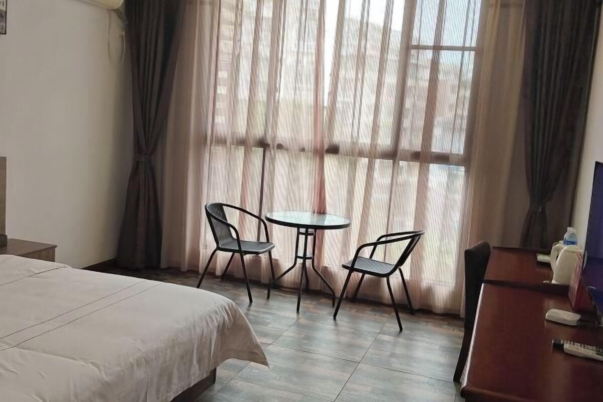 A hotel room with a bed, a small round table with two chairs, a desk with a chair, and a window with curtains.