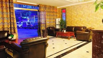 A hotel lobby with leather sofas, a coffee table, and a large window overlooking a parking area.