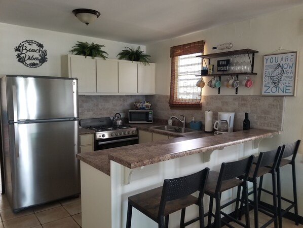 A kitchen with a stainless steel refrigerator, a stove, a microwave, and a sink. There are bar stools and a sign that says "You are now entering a staff-free zone."