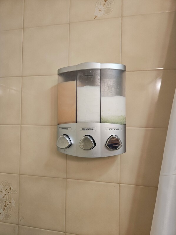 Un distributeur mural doté de trois compartiments étiquetés pour le shampoing, l’après-shampoing et le gel douche.