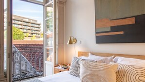 A hotel room with a large bed, a view of a building through a window, and a painting on the wall. - Casa Azul - Santa Marinha (Vila Nova de Gaia)