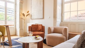 A well-lit living room with a large window, a round coffee table with a plate of food and glasses, and a brown armchair. - Casa Azul - Santa Marinha (Vila Nova de Gaia)
