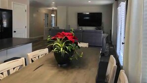 Ein Essbereich mit Holztisch, Stühlen, einem Blumentopf mit roten Blüten und einer Küche im Hintergrund.