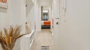 A hallway leading to a bedroom with a bed, a white wall-mounted phone, and a vase with dried plants. - Seagusta - sea view apartment in Middelkerke (Middelkerke)