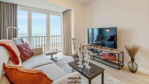 A modern living room with a large TV, a sofa, a coffee table, and a view of the sea through large windows. - Seagusta - sea view apartment in Middelkerke (Middelkerke)