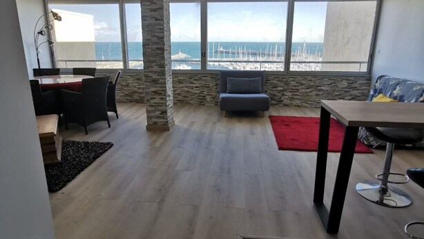 Amplia sala de estar con un ventanal grande que da al mar, un comedor con un tapete rojo y un moderno pilar de piedra.