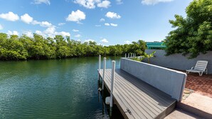 A wooden dock extending into calm water, surrounded by lush greenery and a clear sky. - Ocean Front, Private home with Boat Dock, 3 bedroom (Key West)