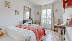 Habitación de hotel con cama, escritorio, silla, espejo y ventana con vistas a edificios.