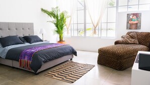 Une chambre à coucher avec un lit, une plante en pot, un fauteuil à motifs léopard et une fenêtre avec des rideaux.