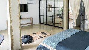 Ein modernes Schlafzimmer mit Bett, großem Fenster und einer Schiebeglastür zu einem Wohnbereich.