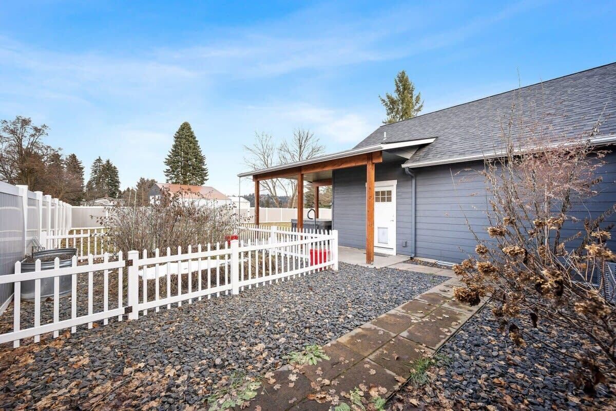 A modern house with a covered porch, a white fence, and a gravel driveway.