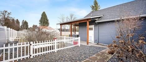 A modern house with a covered porch, a white fence, and a gravel driveway.