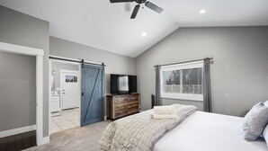 Ein Schlafzimmer mit einem Bett, einem Fernseher auf einer Holzkommode, einem Deckenventilator und einem Fenster mit Jalousien.
