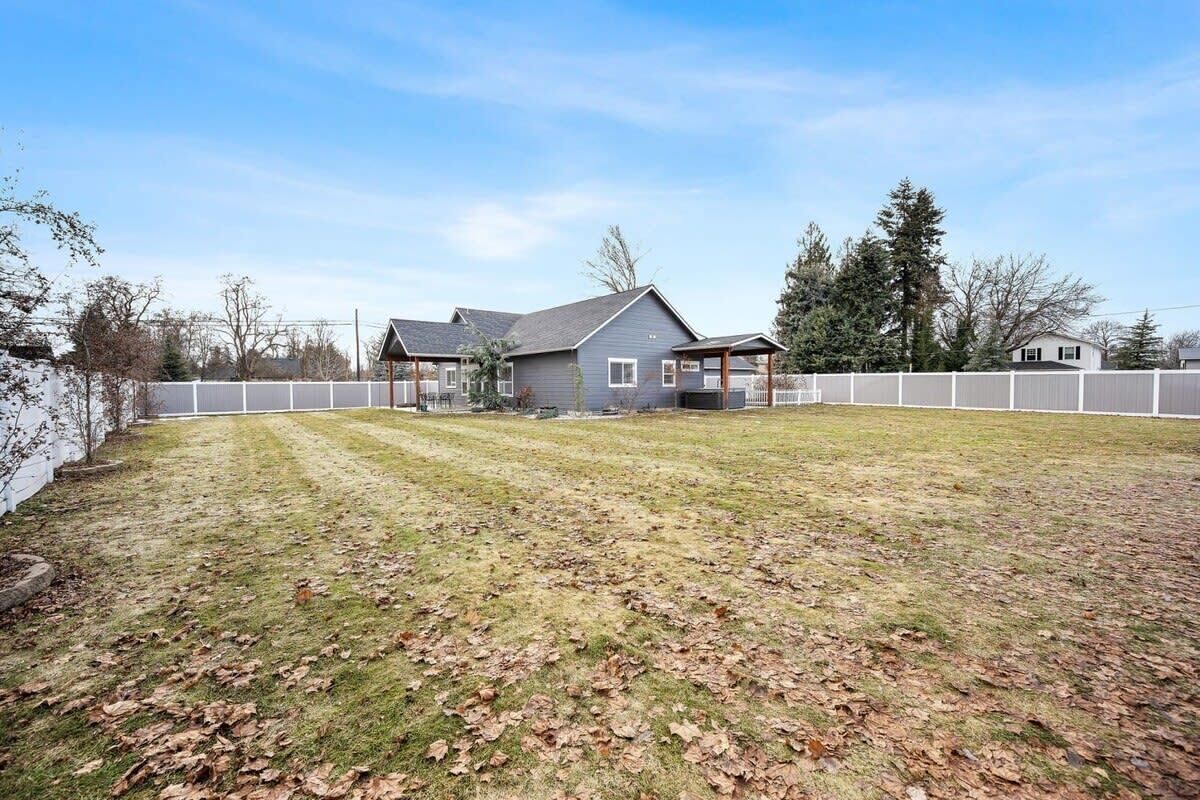 A residential property with a large lawn, a covered porch, and a fenced yard.