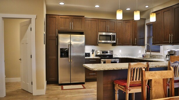A modern kitchen with wooden cabinets, stainless steel appliances, and a central island with seating. - Walk to Train! Pet-Friendly Townhome! (Bryson City)